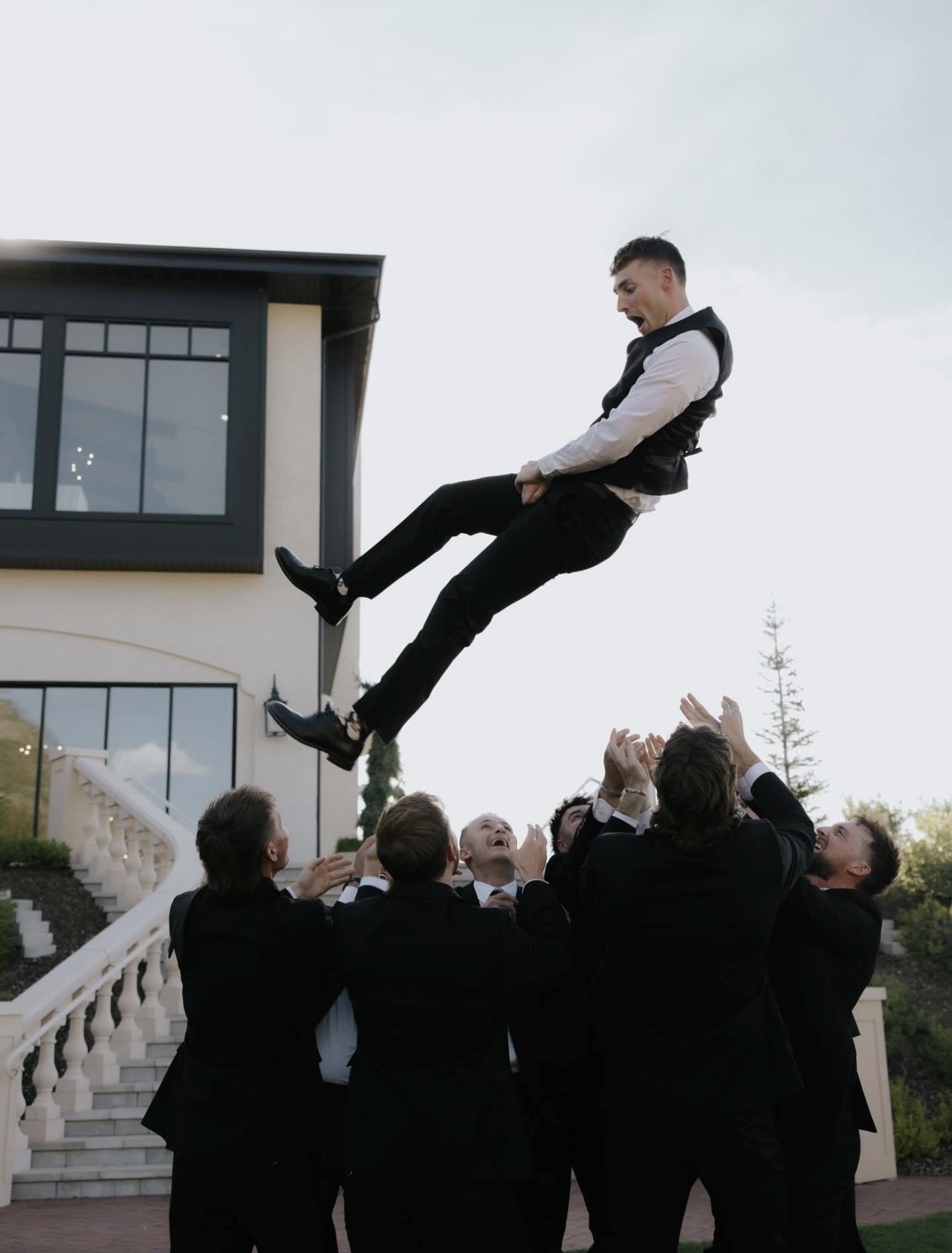 Groomsmen tossing the groom into the air outside the venue
