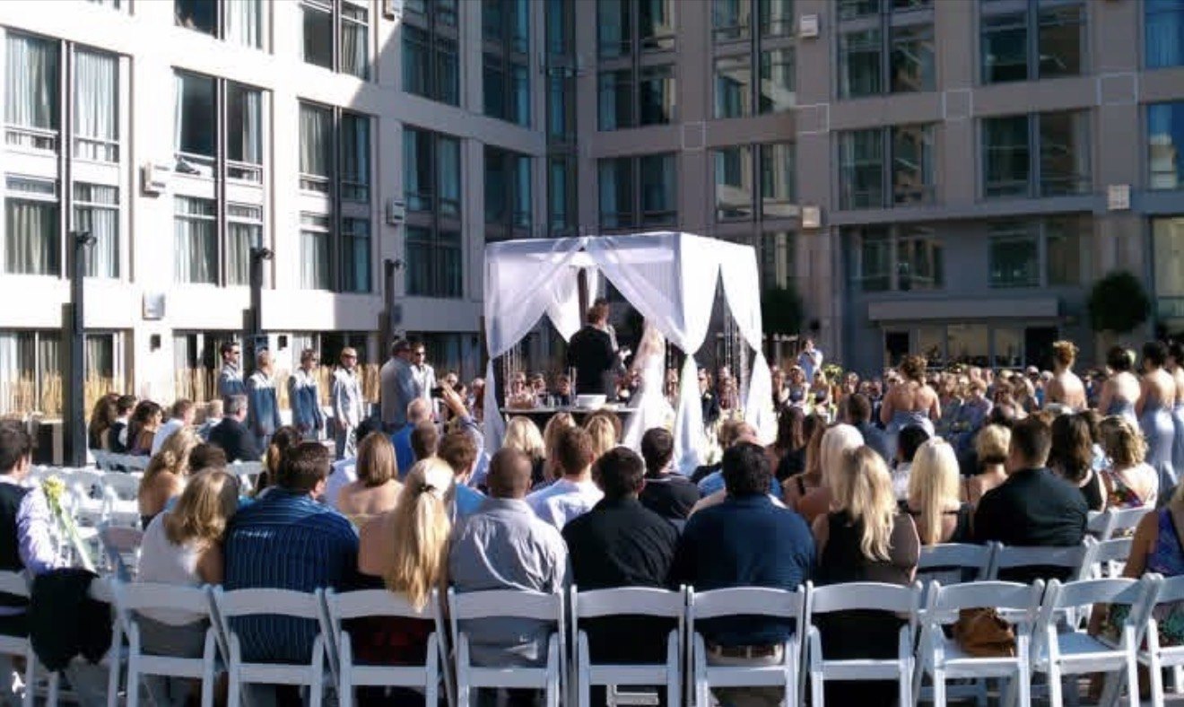 Outdoor courtyard wedding ceremony under a white canopy with seated guests