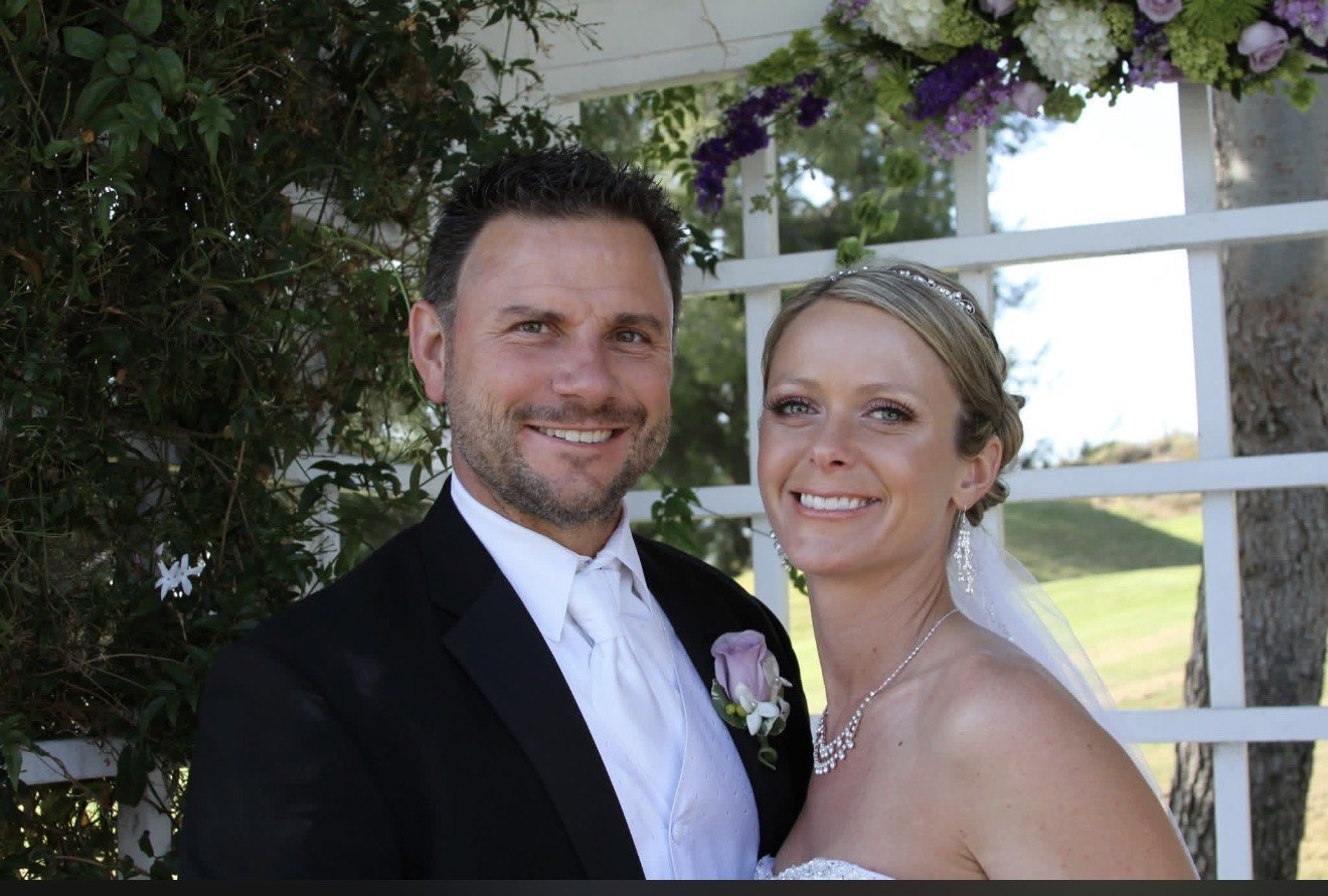 Bride and groom under a white arbor draped in purple and white flowers