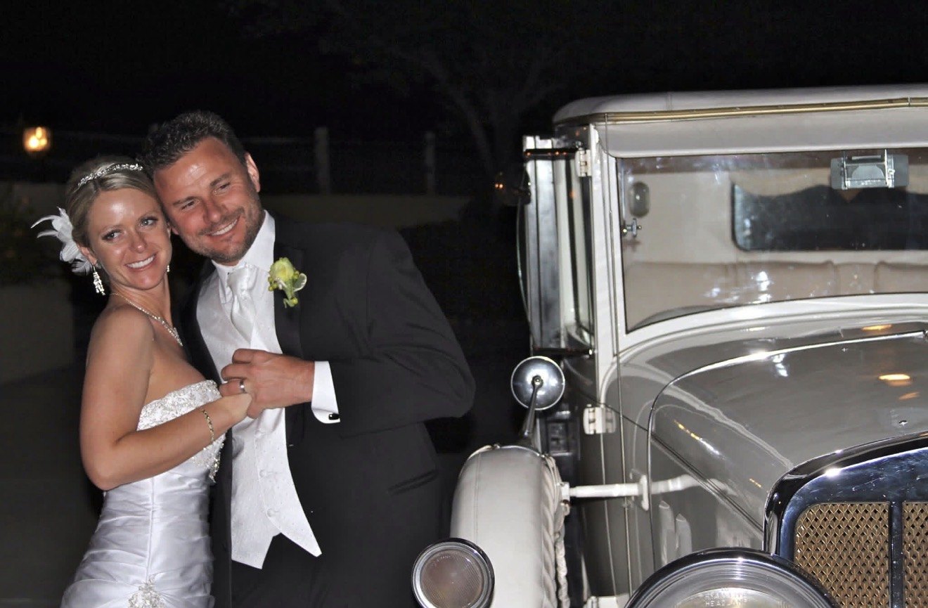 Bride and groom posing beside a vintage getaway car at night