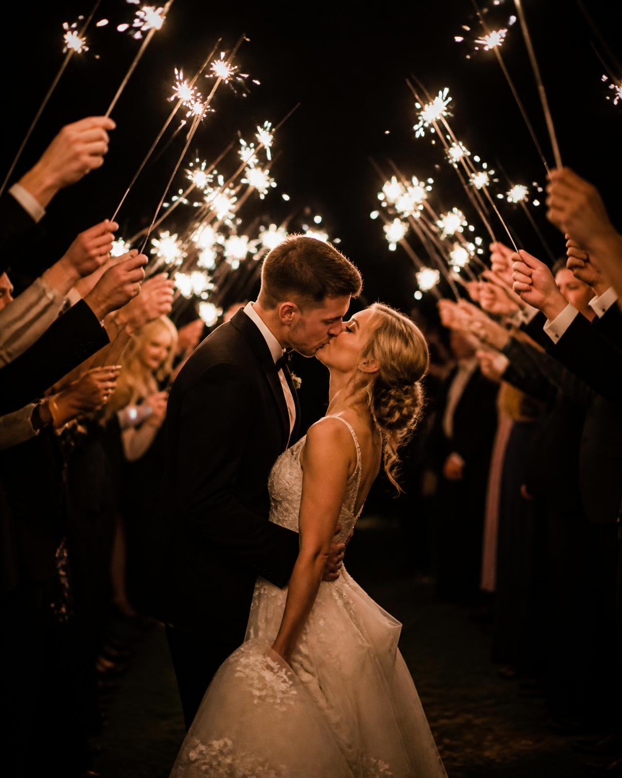 Bride and groom kissing under a sparkler tunnel at night